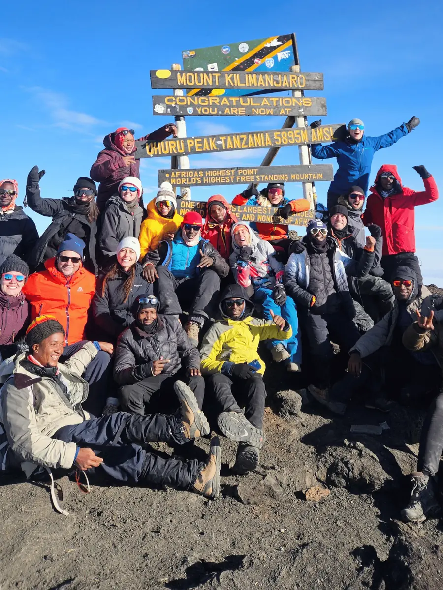 A group celebrating at the Uhuru Peak sign on the summit of Kilimanjaro