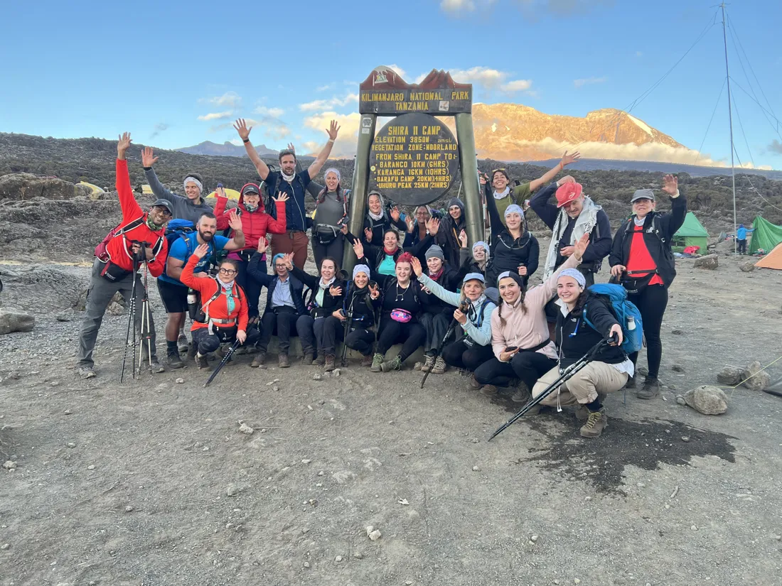 A group celebrating together at a Kilimanjaro camp sign